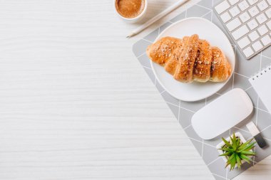 Düzenlenmiş kruvasan, kahve Kupası ve bilgisayar klavye Office ile çalışma alanı'nın üstten görünüm 