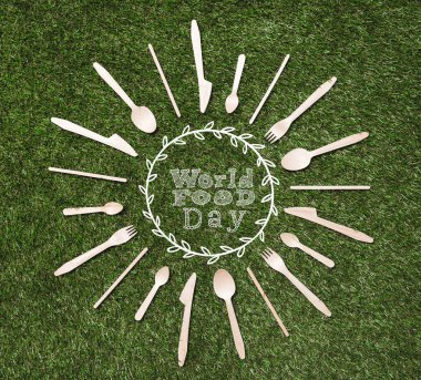 top view of wooden spoons with forks and knives in shape of sun lying on grass, world food day inscription clipart