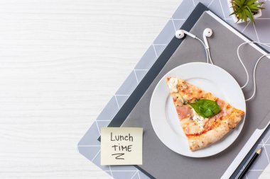 Beyaz ahşap masa üzerinde pizza, kulaklık ve yazıt öğle vakti ile Yapışkan Not üstten görünüm