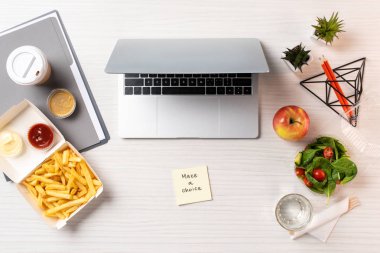 top view of laptop, paper with inscription make a choice and junk food with healthy food on table in office  clipart