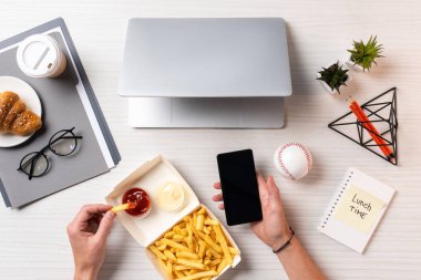 Ketçap ile patates kızartması yemek ve işyerinde boş ekran ile smartphone kullanarak kişi resmini kırpılmış