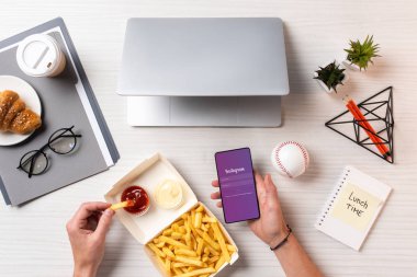 Ketçap ile patates kızartması yemek ve işyerinde instagram app ile smartphone kullanarak kişi resmini kırpılmış