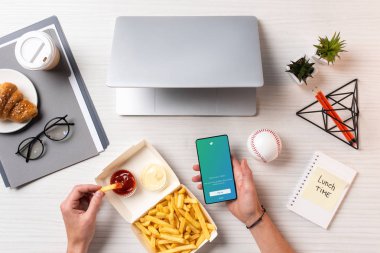 Ketçap ile patates kızartması yemek ve işyerinde twitter uygulaması ile smartphone kullanarak kişi resmini kırpılmış