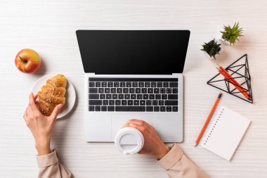 Tek kullanımlık kahve ve kruvasan ile boş ekran dizüstü bilgisayar kullanırken tutan işkadını kırpılmış atış
