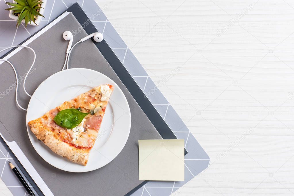 top view of pizza on plate, blank note and earphones on white wooden table