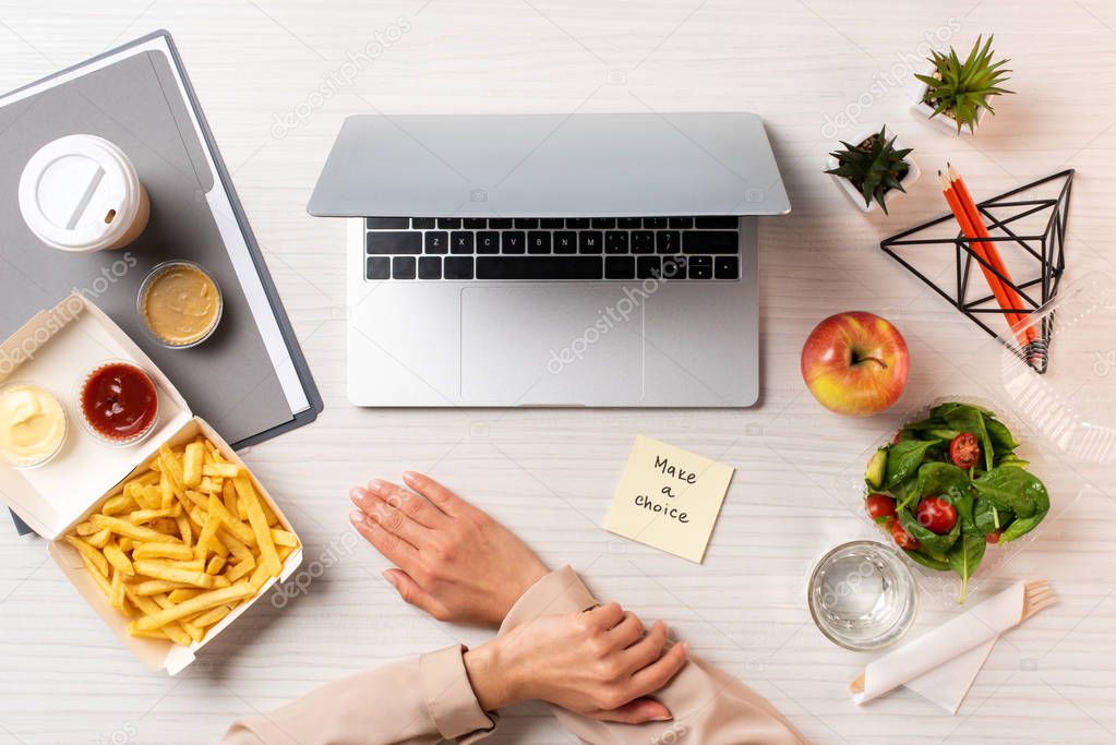 cropped shot of businesswoman, laptop, note with inscription make a choice and healthy food with junk food at workplace 