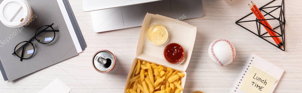 top view of french fries, soda can, baseball ball and office supplies at workplace