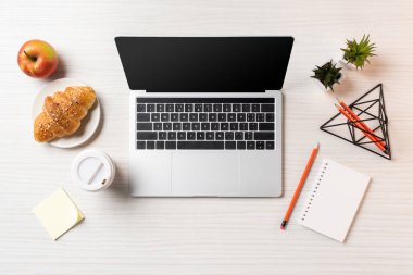Ofis masaları üzerinde boş ekran, kruvasan, elma ve tek kullanımlık kahve fincanı ile dizüstü üstten görünüm   
