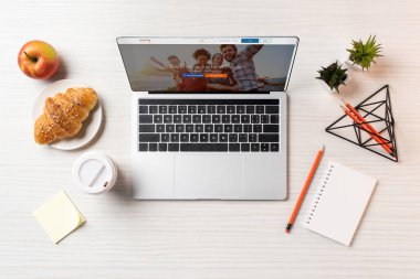 Ofis masaları üzerinde couchsurfing Web sitesi, kruvasan, elma ve tek kullanımlık kahve fincanı ile dizüstü üstten görünüm   