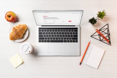 Ofis masaları üzerinde airbnb Web sitesi, kruvasan, elma ve tek kullanımlık kahve fincanı ile dizüstü üstten görünüm  