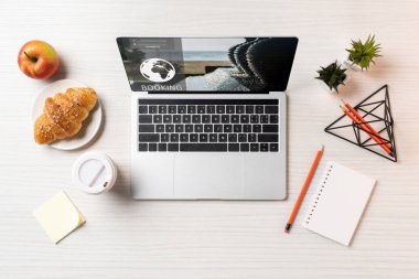 rezervasyon web sitesi, kruvasan, elma ve ofis masası üzerinde kahve ile dizüstü üstten görünüm 