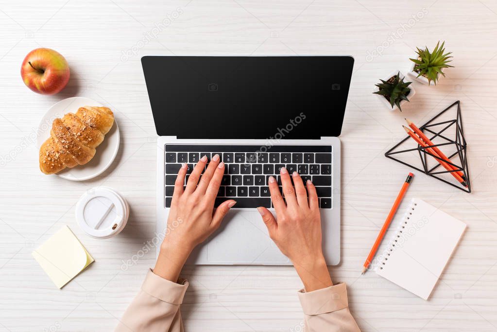 cropped shot of businesswoman using laptop with blank screen at table with coffee, apple and croissant         