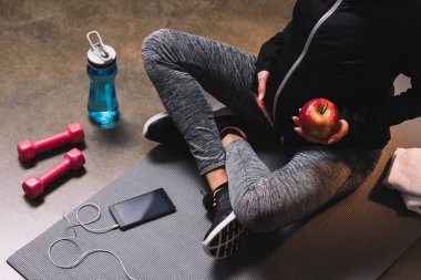 Hamile sportif kadın elinde apple ile sportif mindere oturmuş görünümünü kırpılmış