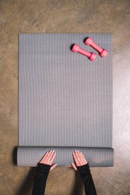 Top view of female hands unfolding sports mat with pink dumbbells clipart