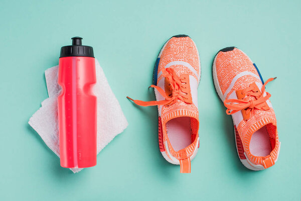 Top view of sneakers, sport bottle and towel on turquoise background