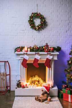 Fireplace with Christmas decorations near Christmas tree with gifts clipart