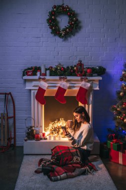 şömine ve Noel ağacı Noel yakınındaki Smartphone kullanarak çekici kadın dekore edilmiş