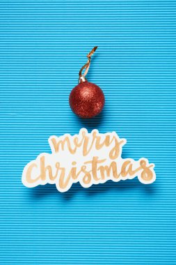 Flat lay of Merry Christmas sign and christmas ball on the blue textured background clipart
