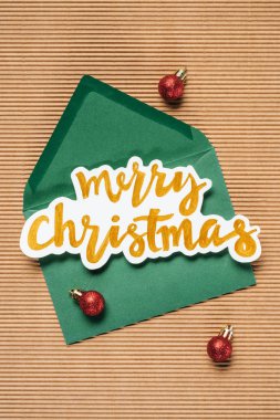 Flat lay of green envelope with Merry Christmas sign and red Christmas balls on the textured background clipart