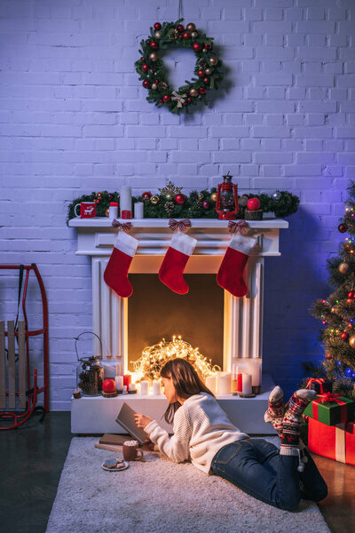 Adorable woman reading near christmas decorated fireplace and Christmas tree