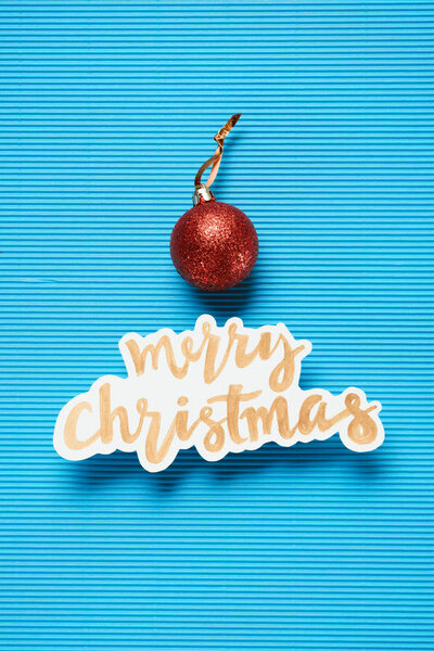 Flat lay of Merry Christmas sign and christmas ball on the blue textured background
