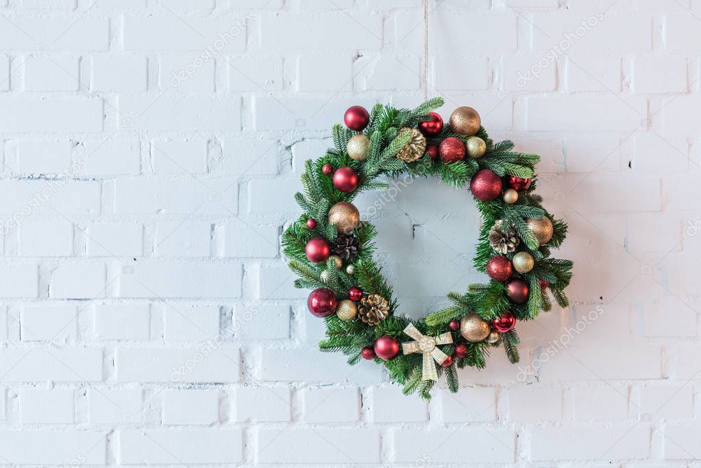 Christmas wreath decorated with balls and bow on the background of white brick wall