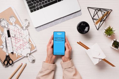 Ofis Masası skype uygulaması ile akıllı telefon ekranında, düz tutarak laptop ve kadın elleriyle yatıyordu