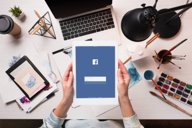 Tasarımcı holding tablet ile facebook app görünümünü sanat malzemeleri ile ofis masası, ekranda kırpılmış, düz yatıyordu