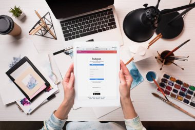 Tasarımcı holding tablet ile instagram app görünümünü sanat malzemeleri ile ofis masası, ekranda kırpılmış, düz yatıyordu