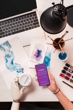 Tasarımcı ofis masası, kırpılmış kadın el smartphone instagram app ile ekranda tutan robot el ile üstten görünüm