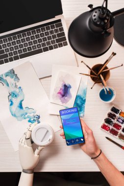 smartphone ile rezervasyon app ekranda tutan robot el ile görünümü tasarımcısının ofis masası, kırpılmış
