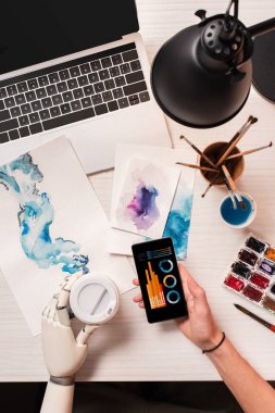 smartphone ile grafik ekran üzerinde tutan robot el ile görünümü tasarımcısının ofis masası, kırpılmış