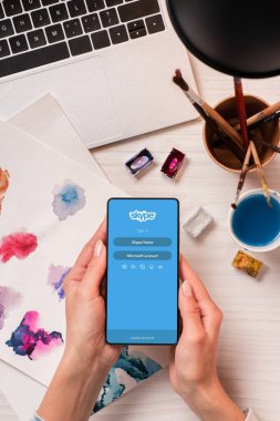 Görünüm Tasarımcısı smartphone skype uygulaması ile ekran üzerinde tutarak ofis masası, kırpılmış, düz yatıyordu