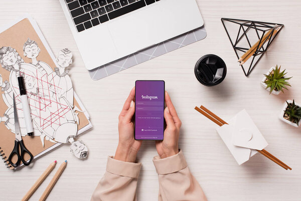 office desk with laptop and woman hands holding smartphone with instagram app on screen, flat lay