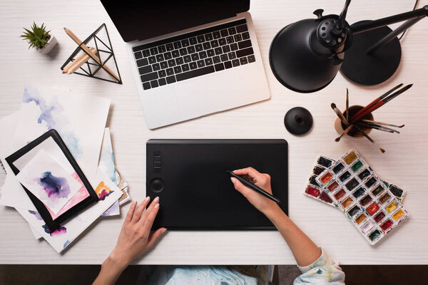 office desk with laptop, art supplies and cropped view of designer using graphics tablet and pen, flat lay