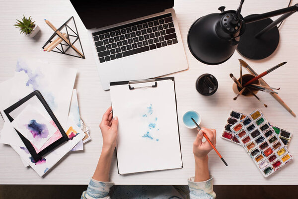 office desk with laptop, art supplies and cropped view of designer drawing, flat lay