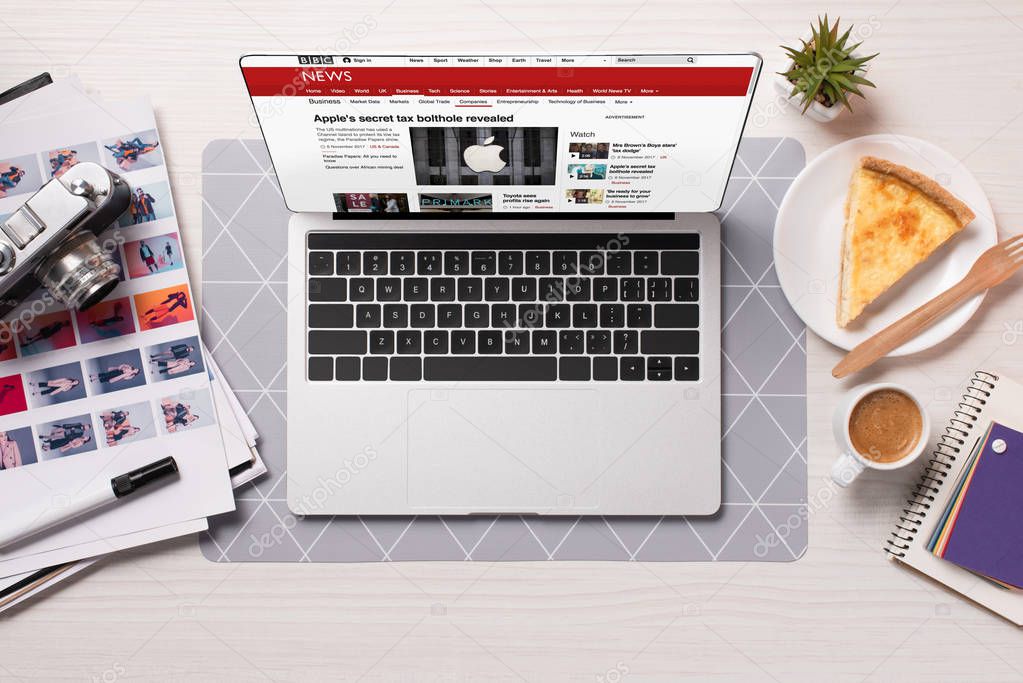 Office desk with laptop and bbc news website on screen, flat lay