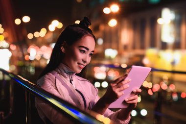 akşam, gelecekteki kavramının şehir neon ışık ile sokakta tablet kullanarak çekici Asyalı kız