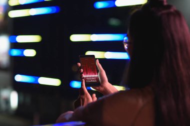 arkadan görünüşü akşamlar, gelecekteki kavramının şehir kursları cihazı ile neon ışık Caddesi üzerinde ticari smartphone tutan kız