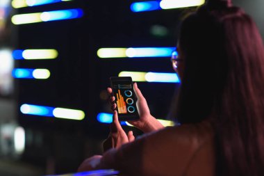 arkadan görünüşü akşamlar, gelecekteki kavramının şehir sokak neon ışık ile taşıma aracı ile smartphone tutan kız