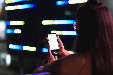 arkadan görünüşü akşamlar, gelecekteki kavramının şehir smartphone ile boş bir beyaz ekran ile neon ışık Caddesi üzerinde tutan kız