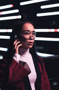 Bordo kimono ve kablosuz kulaklık uzağa sokakta akşam, gelecekteki kavramının şehir neon ışık ile seyir çekici Asyalı kız