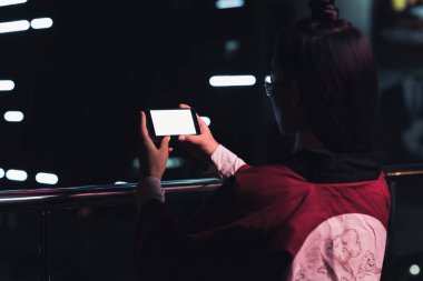 arkadan görünüşü akşamlar, gelecekteki kavramının şehir smartphone ile boş bir beyaz ekran ile neon ışık Caddesi üzerinde tutan kız