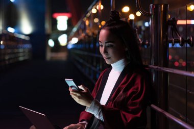 oturma ve neon ışık, gelecekteki kavramının şehir sokakta smartphone ile dizüstü bilgisayar kullanarak kimono içinde çekici Asyalı kız