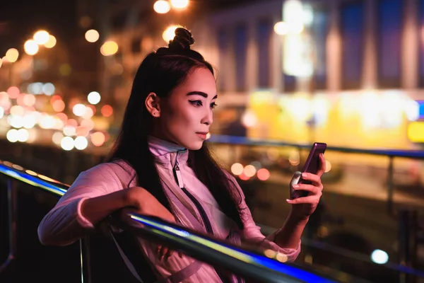 有吸引力的亚洲女孩使用智能手机在街上与霓虹灯在晚上 未来概念的城市 — 图库照片