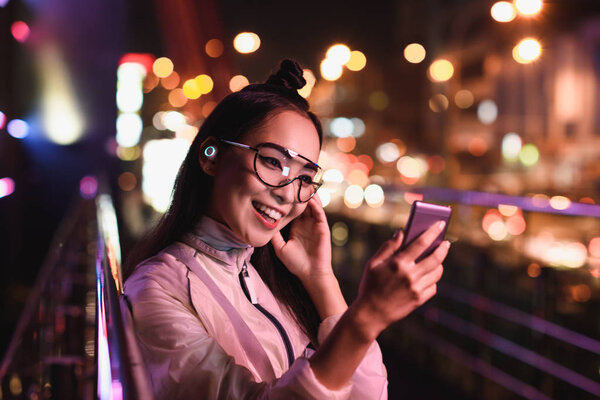 happy asian girl having video chat and using smartphone on street with neon light, city of future concept