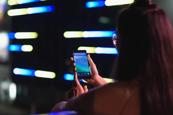 女孩拿着智能手机与预订用具在街上与霓虹灯在晚上的背景图 未来概念的城市 — 图库照片