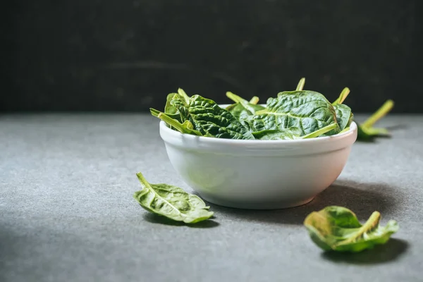Vegetarian spinach leaves in white bowl on grey background