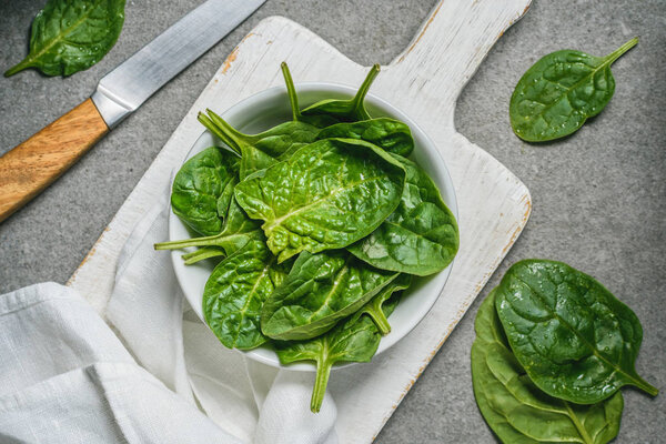 Top view of green spinach leaves in bowl on white cutting board 