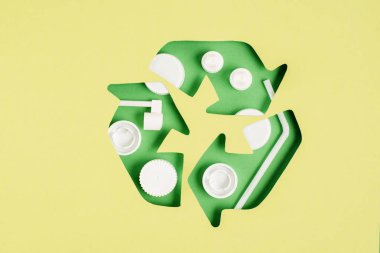 Top view of green recycle sign with bottle caps pattern on yellow background clipart